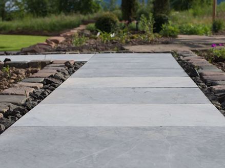 Blausteinplatten als Gartenweg, daneben Beete und im Hintergrund ein grüner Rasen