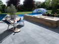 Ein eleganter Stein für eine moderne Terrasse! Frau entspannt auf einer Liege auf Terrasse mit Kalksteinplatten, im Hintergrund ein Garten mit Pool