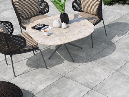Terrasse mit Stuhl und Sesseln, als Bodenbelag helle Platten aus Feinsteinzeug in Betonoptik
