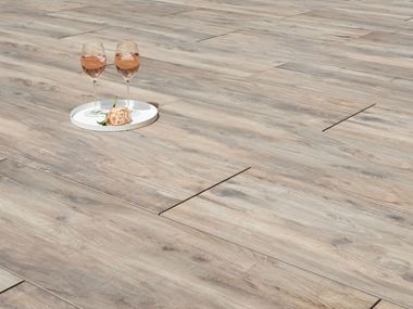 Zwei Weingläser und eine Blume auf Terrassenplatten in Holzoptik