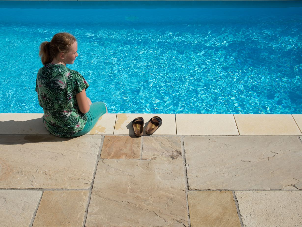 Mädchen sitzt an blauem Pool mit Sandsteinplatten Yellow Mint