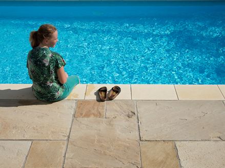 Mädchen sitzt an blauem Pool mit Sandsteinplatten Yellow Mint