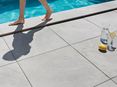 Füsse laufen barfuß auf der Poolumrandung aus Feinsteinzeug-Platten Alpine Grey