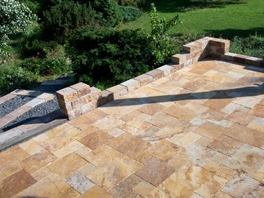 Travertinplatte Gold im Römischen Verband verlegt mit Natursteinmauer und angrenzendem Garten