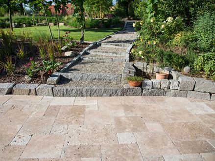 Im Vordergrund Terrasse mit Travertin Noce, als Beeteinfassung Granit, im Hintergrund ein Garten