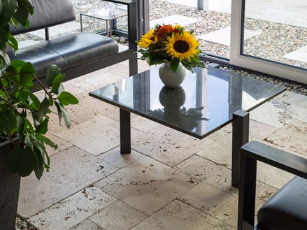 Lebendiger Travertin verbindet in Beige in einem modernen Wintergarten mit Glastisch und Blumenvase