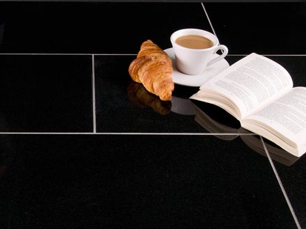 Tasse Kaffee, Croissant und ein aufgeschlagenes Buch auf dunklen Granitfliesen mit hellen Fugen