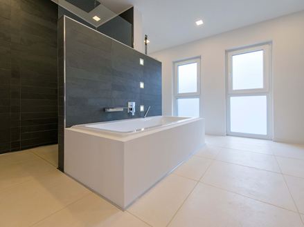 Badewanne auf hellen Kalksteinfliesen und Schiefer als Wandverblender