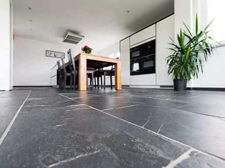 Froschperspektive auf Schieferboden Black Rustic mit Holzesstisch und Pflanze im Hintergrund