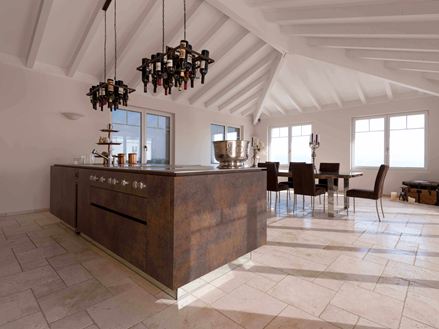 Kücheninsel mit Weinflaschenhalterung an der Decke, im Hintergrund Esstisch und Stühle auf verlegtem Travertin Light mit getrommelter, ungespachtelter Oberfläche