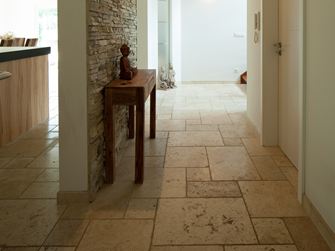 Gang mit Travertinfliese Light als Bodenbelag, kleinem Holztisch und Natursteinverblender an einer Wand