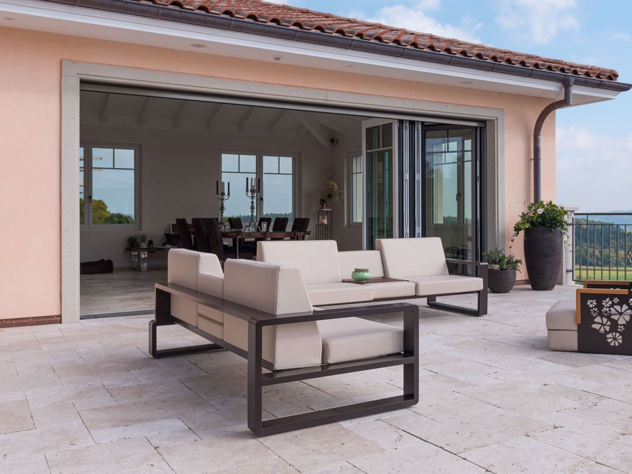 Terrasse mit modernen Gartenmöbeln und breiter Glasfront in den Innenbereich auf Travertinplatte Light