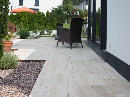 Moderne Terrasse mit Travertinplatten Natura in Holzoptik und dunklen Korbmöbeln