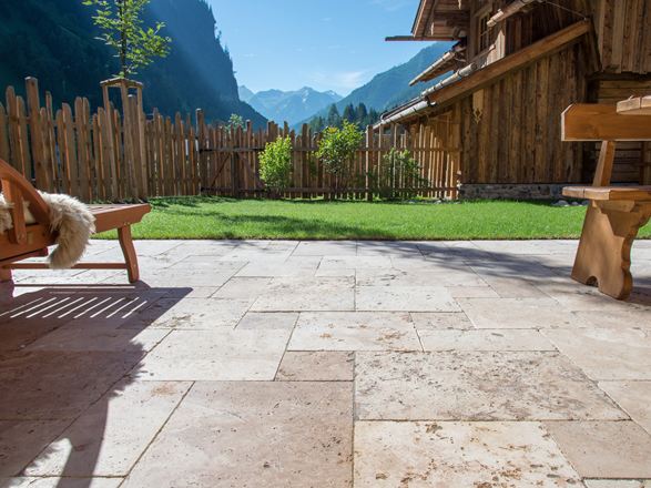 Terrassenboden mit Travertin Rustic und Holzmöbeln, im Hintergrund eine Rasenfläche und Ausblick auf die Berge