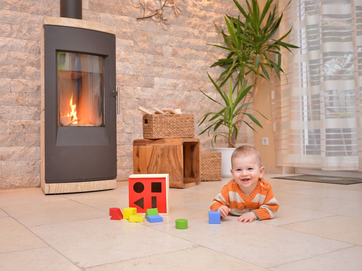 Baby spielt auf Natursteinboden vor einem Kamin