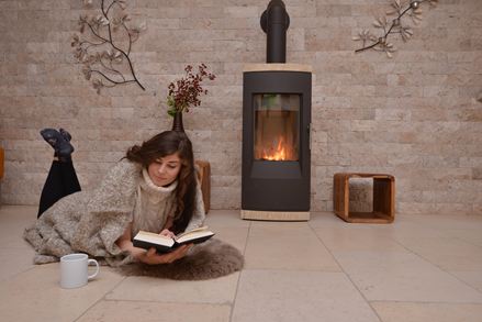 Frau liegt auf Kalksteinfliesen vor einer Wand mit Natursteinverblender und Kamin und liest ein Buch