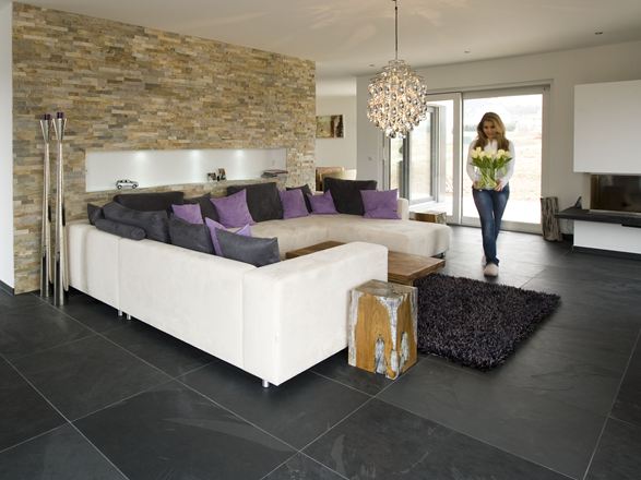 Modernes Wohnzimmer mit Natursteinverblender an der Wand, Schieferfliesen als Bodenbelag und einer weißen Couch