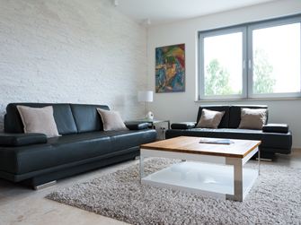 Wohnzimmer mit Naturstein-Verblendern an der Wand und einem schwarzen Sofa